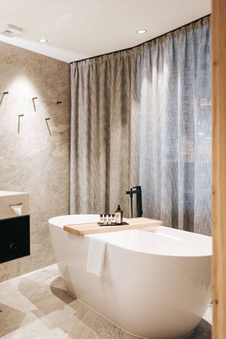 Elegant badeværelse med fritstående badekar, naturmaterialer og minimalistisk alpint design på Hotel Schneider i Obertauern